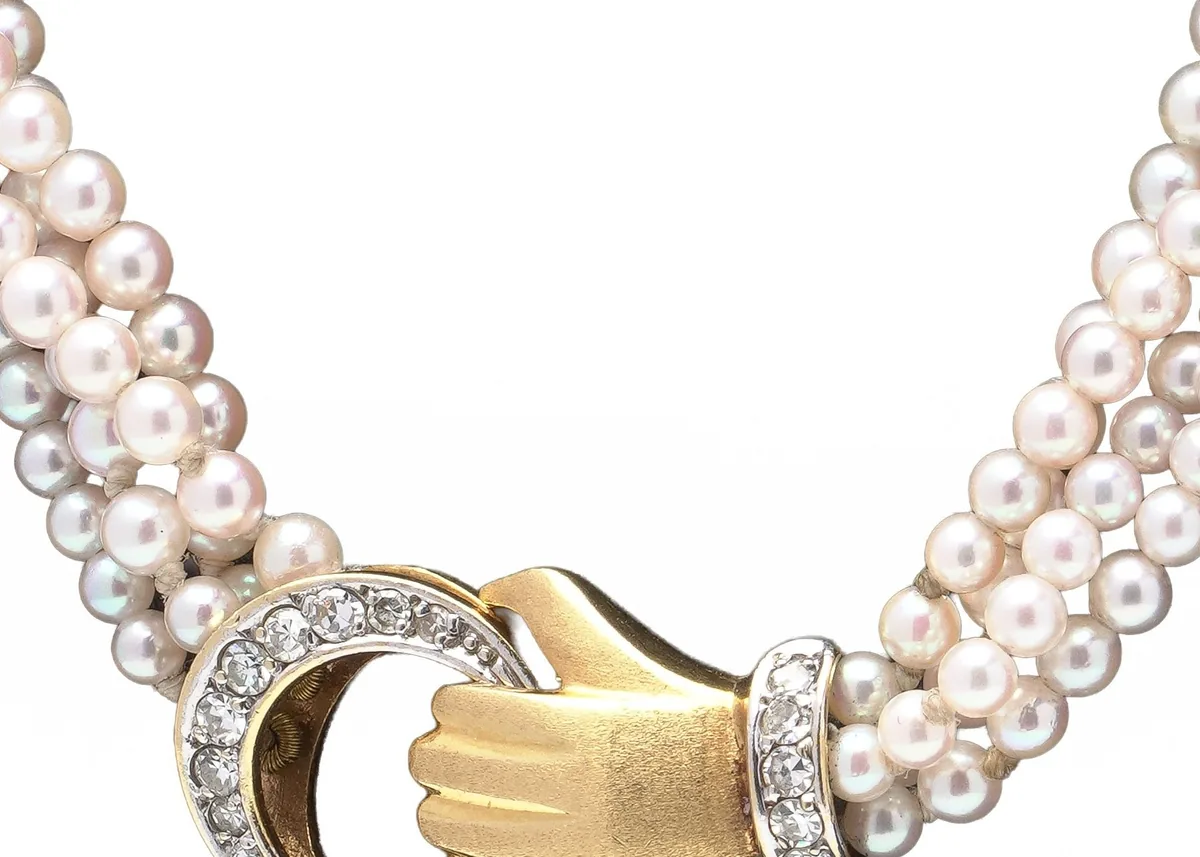Figural 18KT gold clasp in the form of a hand holding a diamond-set ring, on a multi strand seed pearl necklace