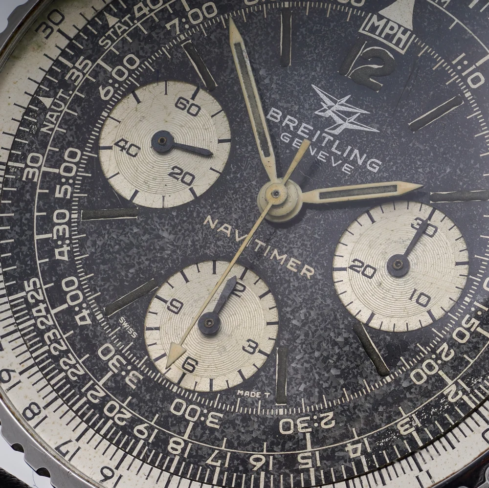 Close-up of a 1960s Navitimer dial: speckled black surface, cream sub-dials with circular graining, gold-toned hands