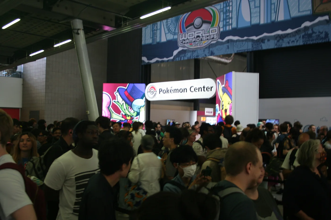 Crowds at the entrance to the 2022 Pokémon World Championships in London, with the World Championships banner and a Pokémon Center pop-up shop