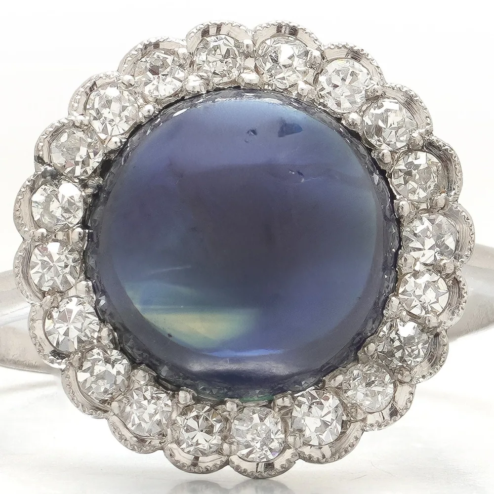 Close-up of an Art Deco platinum cluster ring: a domed cabochon sapphire ringed by twenty-two old cut diamonds in millegrained collets
