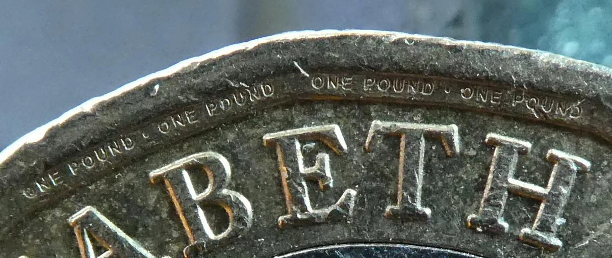 Close-up of the rim of a 12-sided pound coin with tiny ONE POUND micro-lettering inside the rim