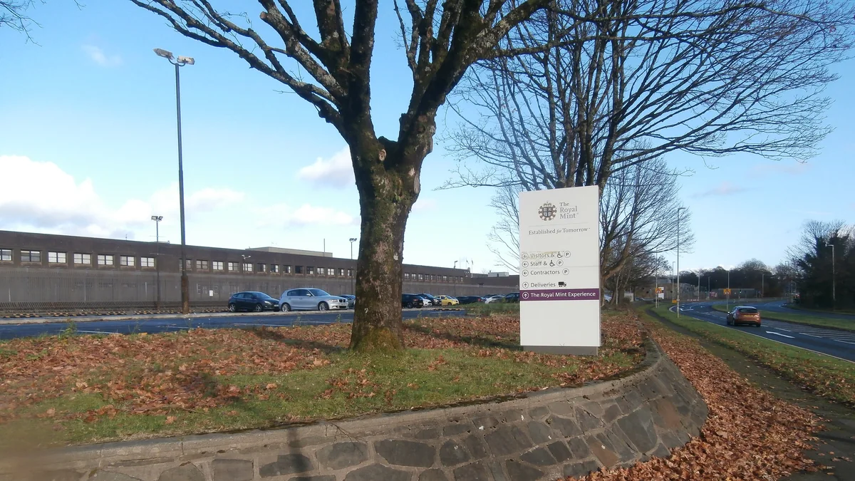 The Royal Mint site at Llantrisant, South Wales, with its entrance sign, trees and the long factory building