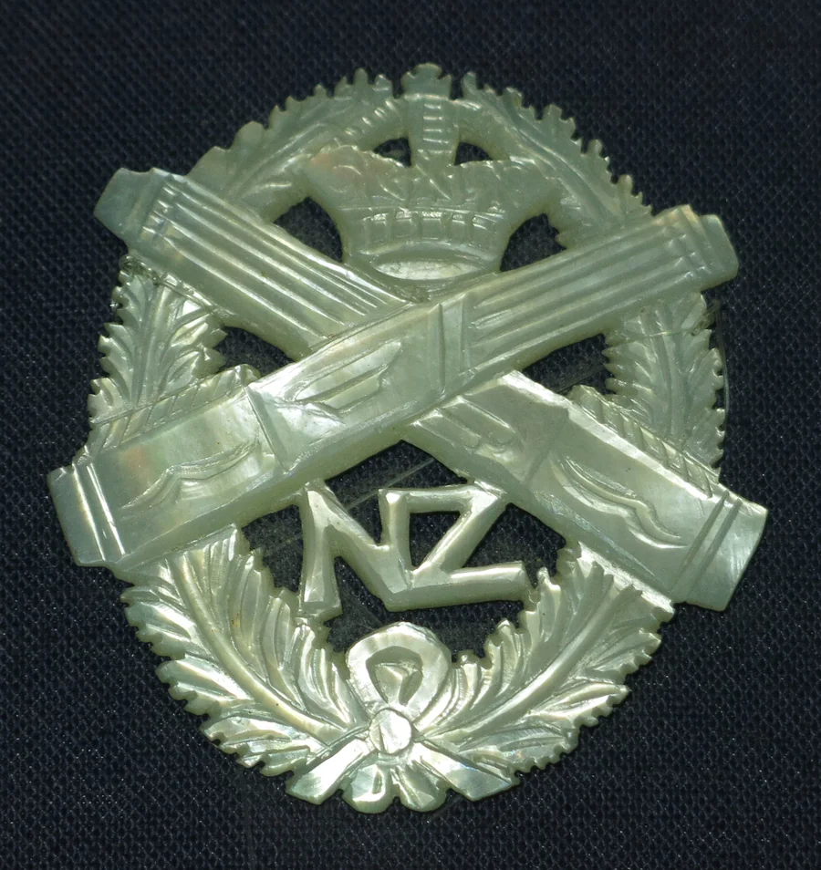 A carved mother of pearl sweetheart brooch made in Bethlehem in 1918: a crown above crossed tubes and the letters NZ inside a carved wreath