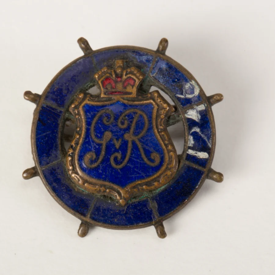 A First World War naval sweetheart brooch: the royal cypher GR on a blue enamel shield set on a ship's steering wheel, with a crown above
