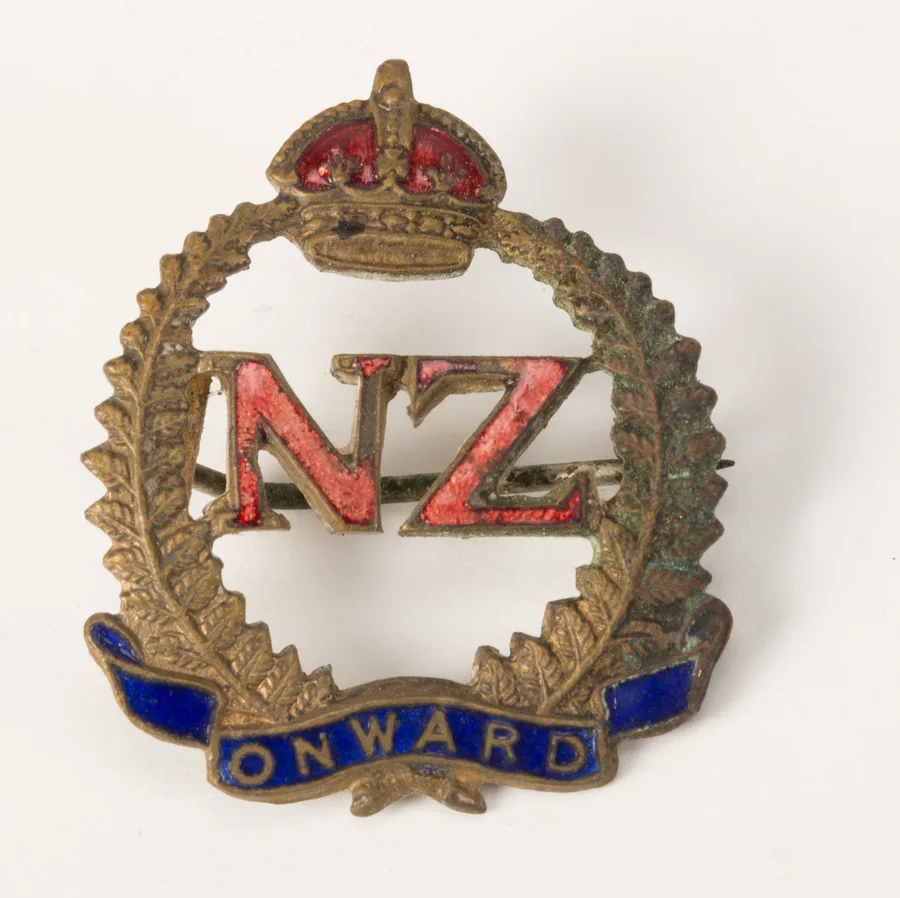 A Second World War brass and enamel sweetheart brooch: red enamel letters NZ inside a fern wreath under a crown, with ONWARD on a blue enamel scroll