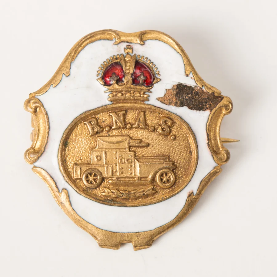 A First World War Royal Naval Air Service armoured car sweetheart brooch: a gilt armoured car on a white enamel plaque under a red enamelled crown, lettered R.N.A.S.