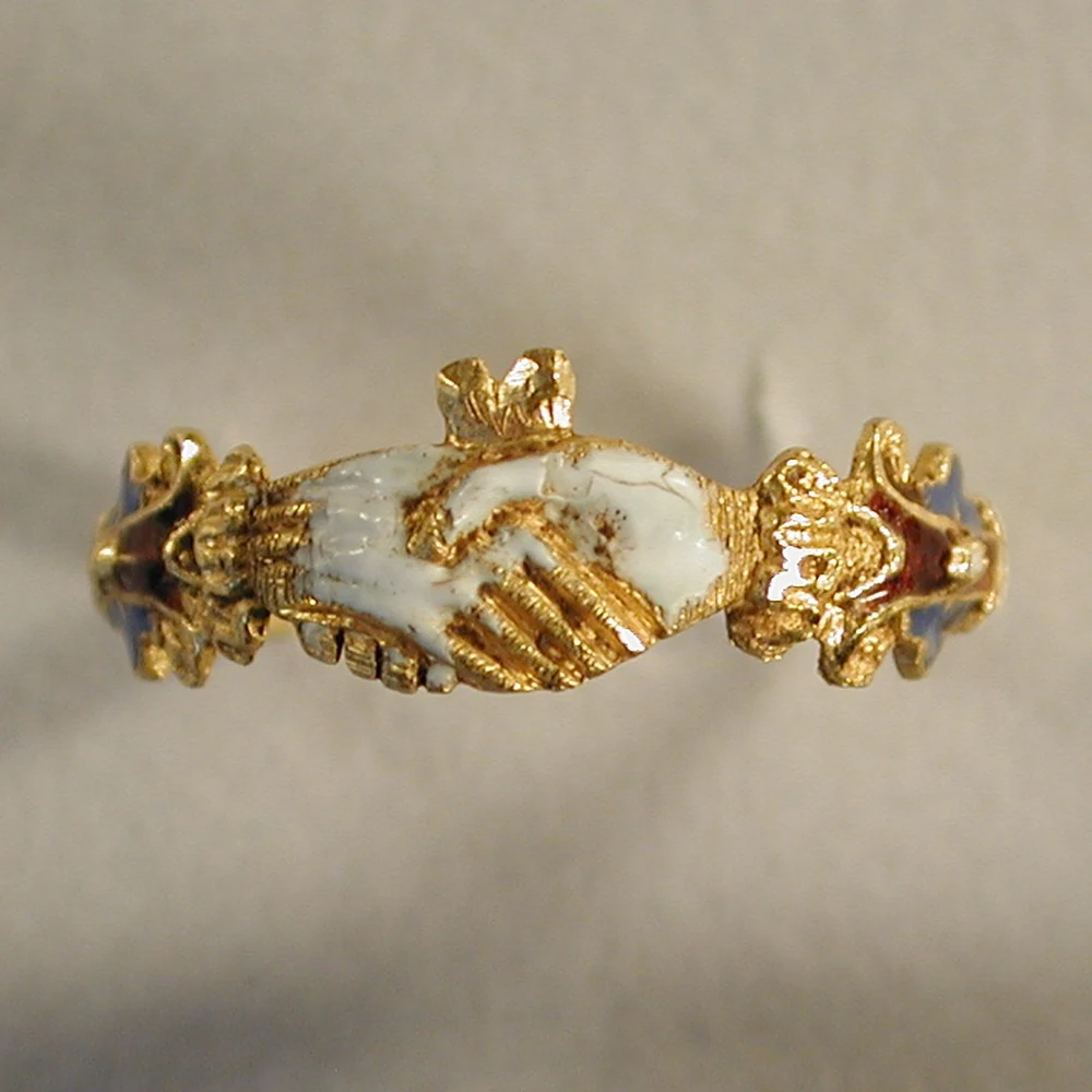A gold fede ring with white enamelled clasped hands and blue, red and white enamel shoulders, found in the Chelmsford area of Essex