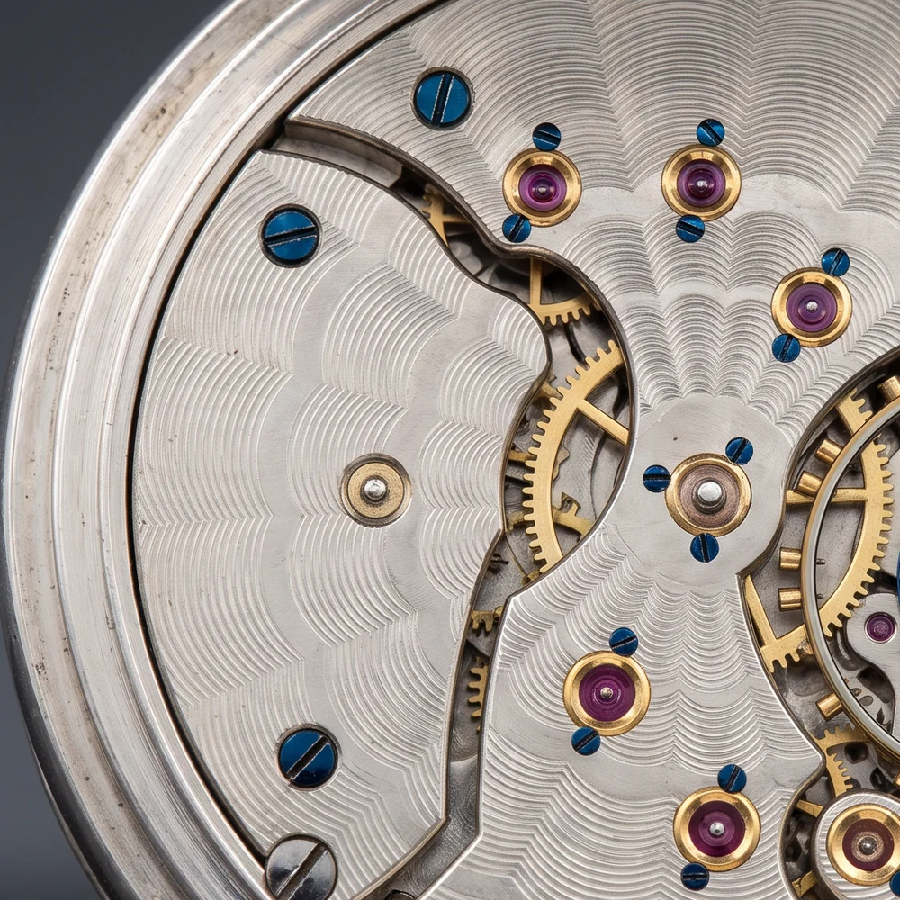 Close-up of a nickel pocket watch movement with damaskeened plates, ruby jewels in gold settings and blued screws