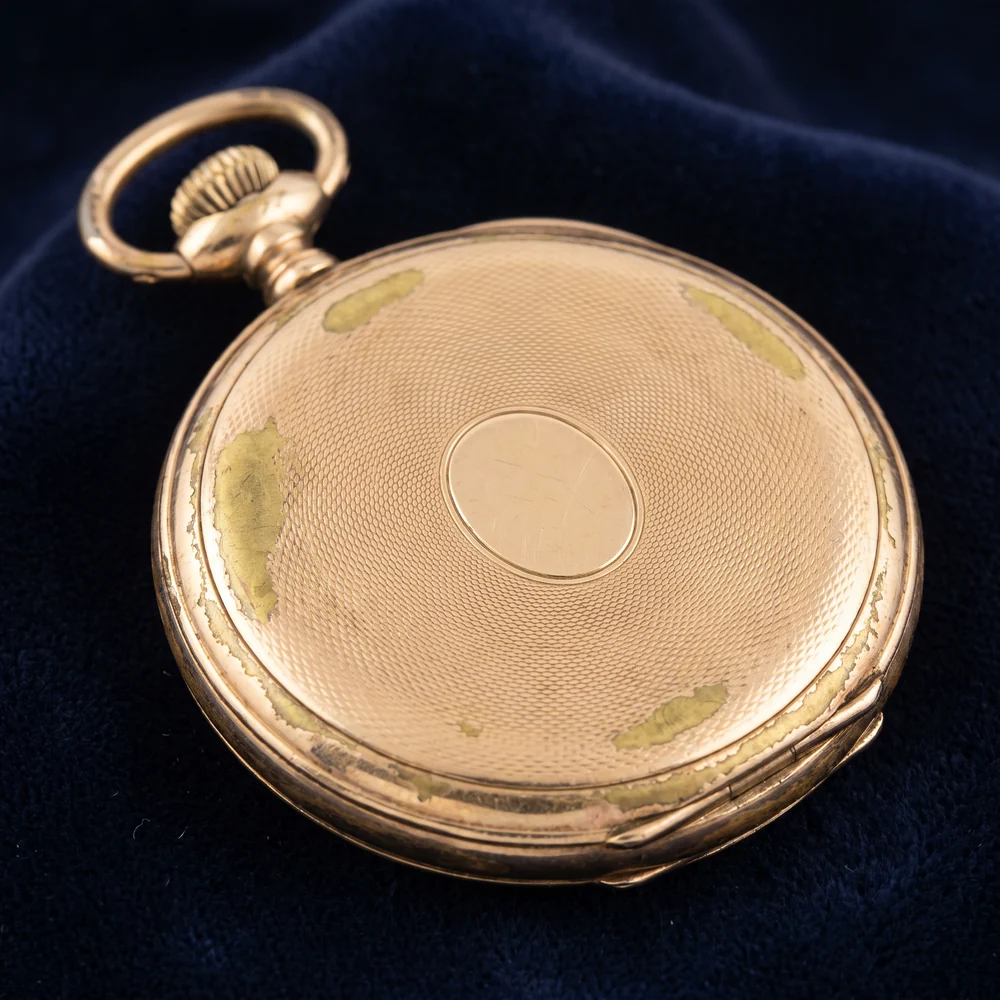 Back of a worn gold filled hunter pocket watch case with brass base metal showing through at the edges