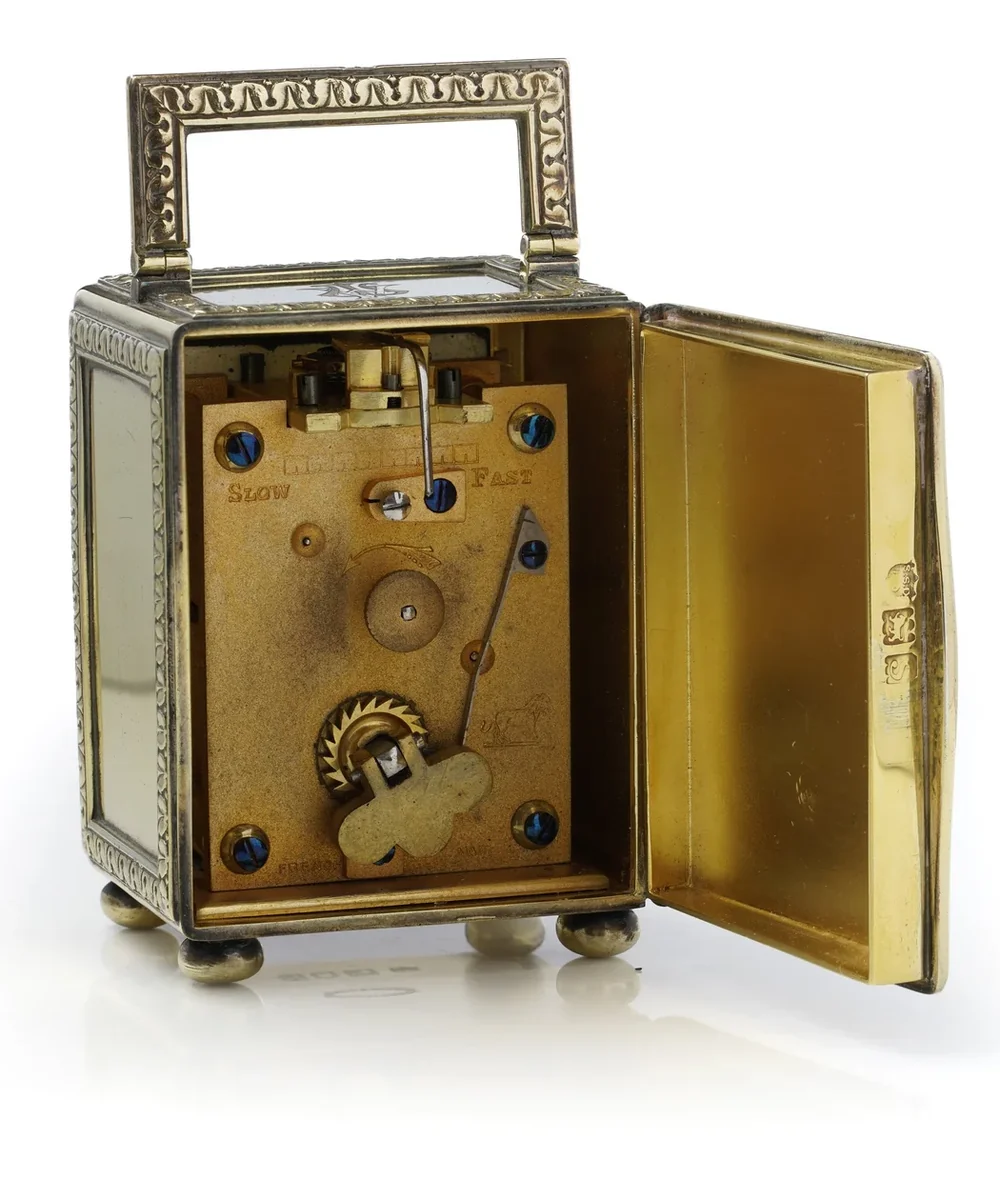 The back door of an Edwardian silver-gilt carriage clock opened on its movement and winding squares