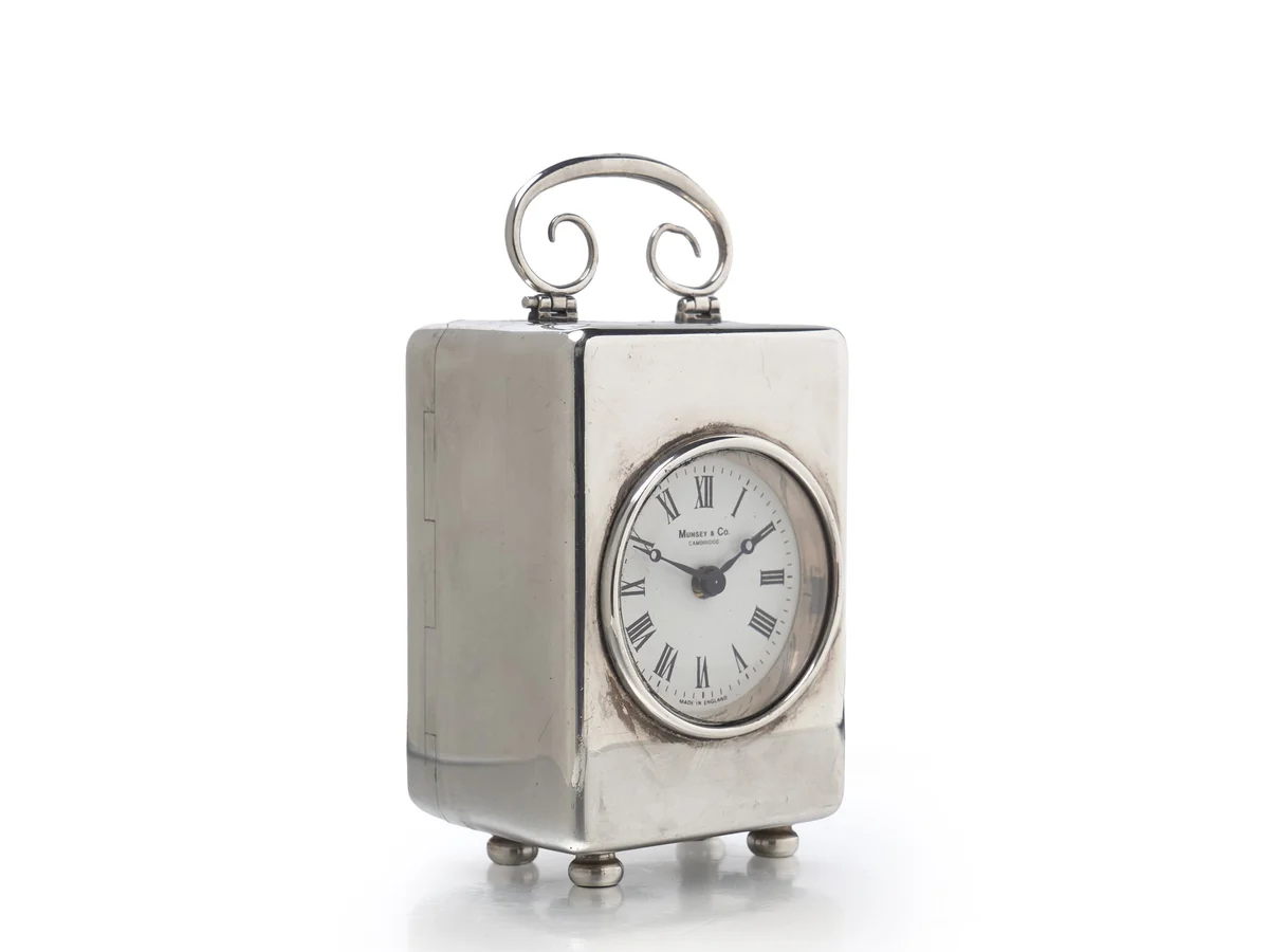 A small silver carriage clock with a white enamel dial, its hands close behind the glass
