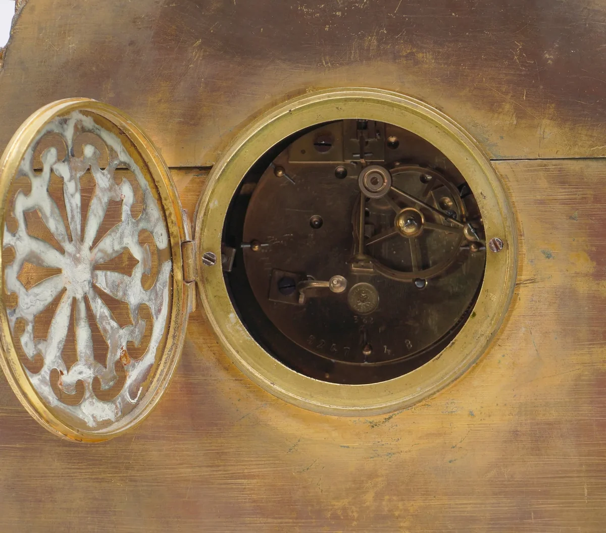 The round back door of a French gilt bronze mantel clock opened on the movement, where the pendulum hangs