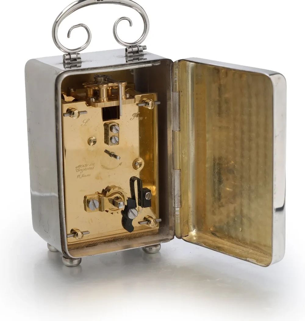 The original movement of a silver carriage clock behind its open back door