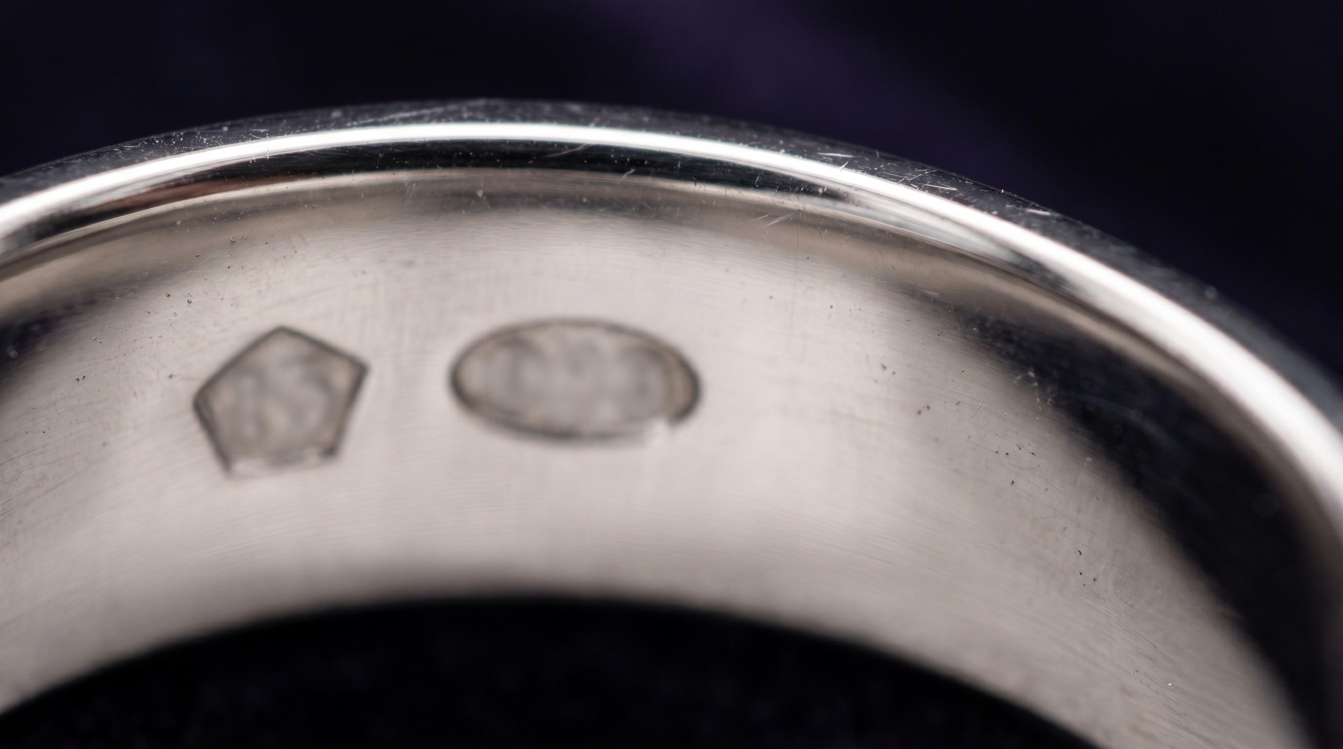 Pentagon-shaped platinum hallmark beside an oval gold mark inside a ring band