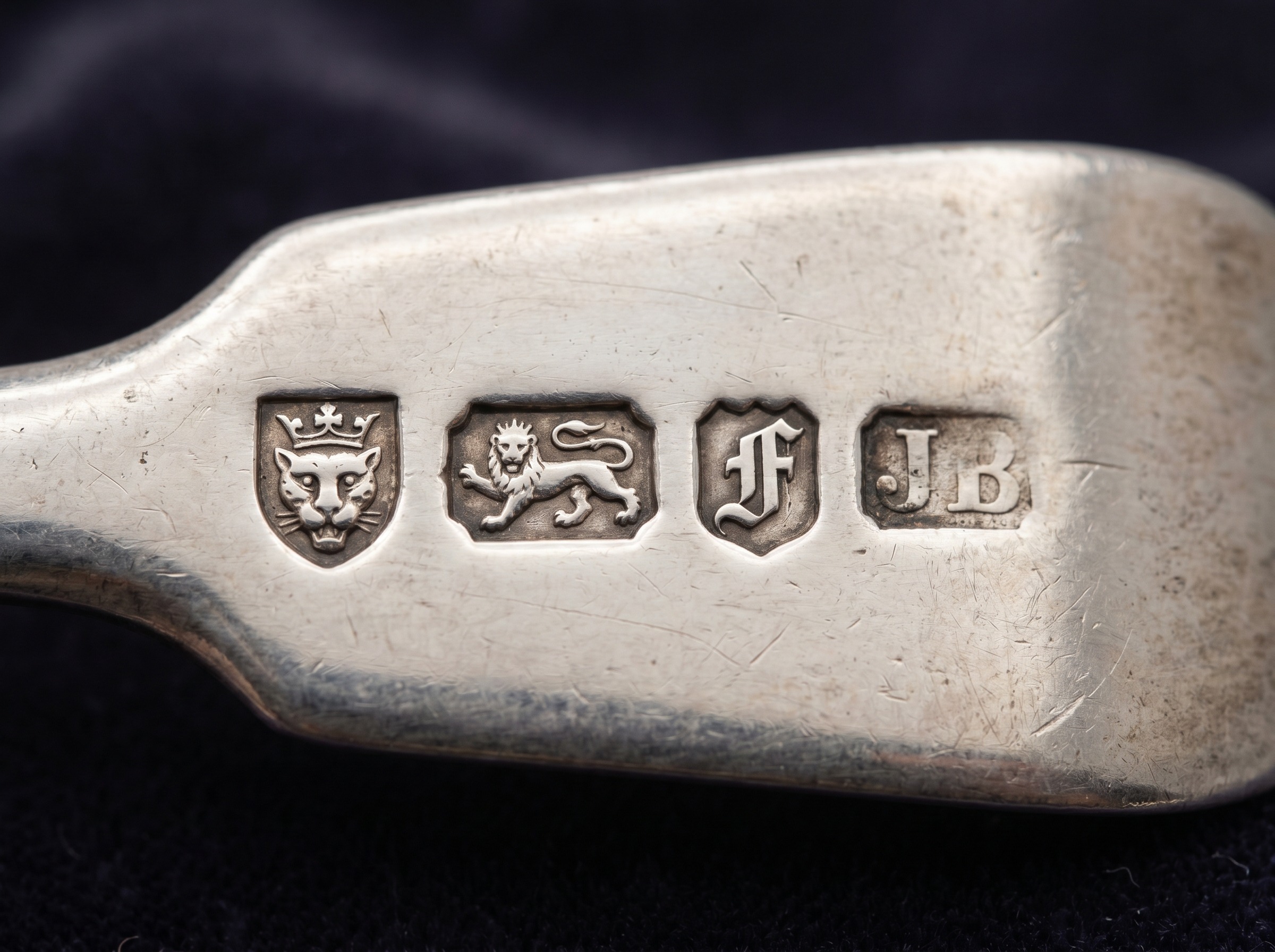 Extreme macro of a full Newcastle hallmark row — three castles, lion passant, date letter and maker's mark