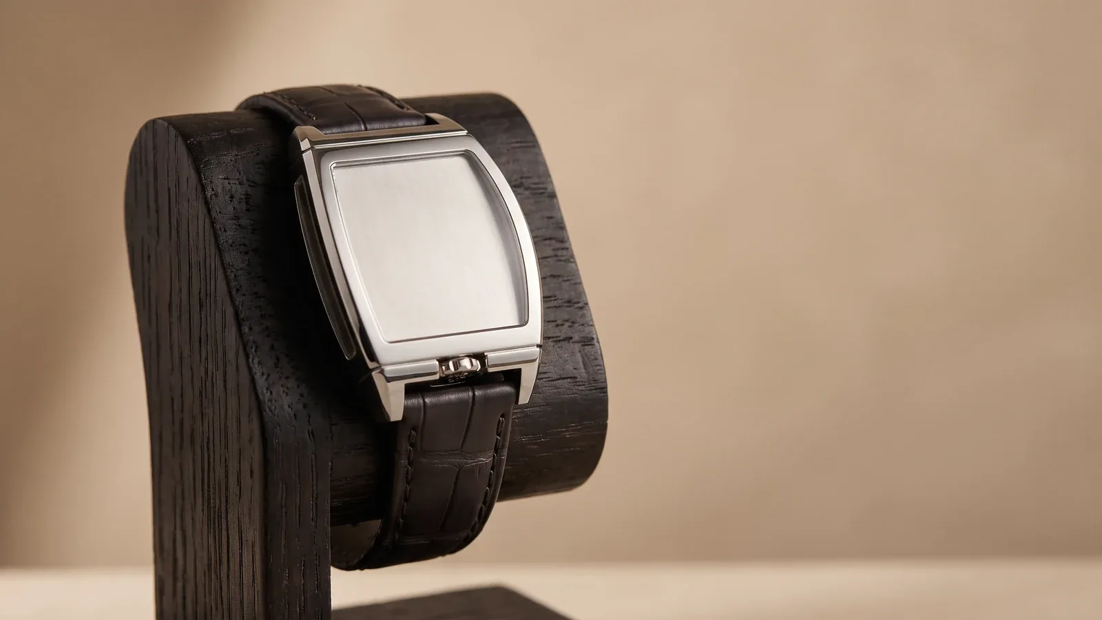 An independent platinum-coloured wristwatch on a dark display stand, three-quarter view, with a plain unmarked dial