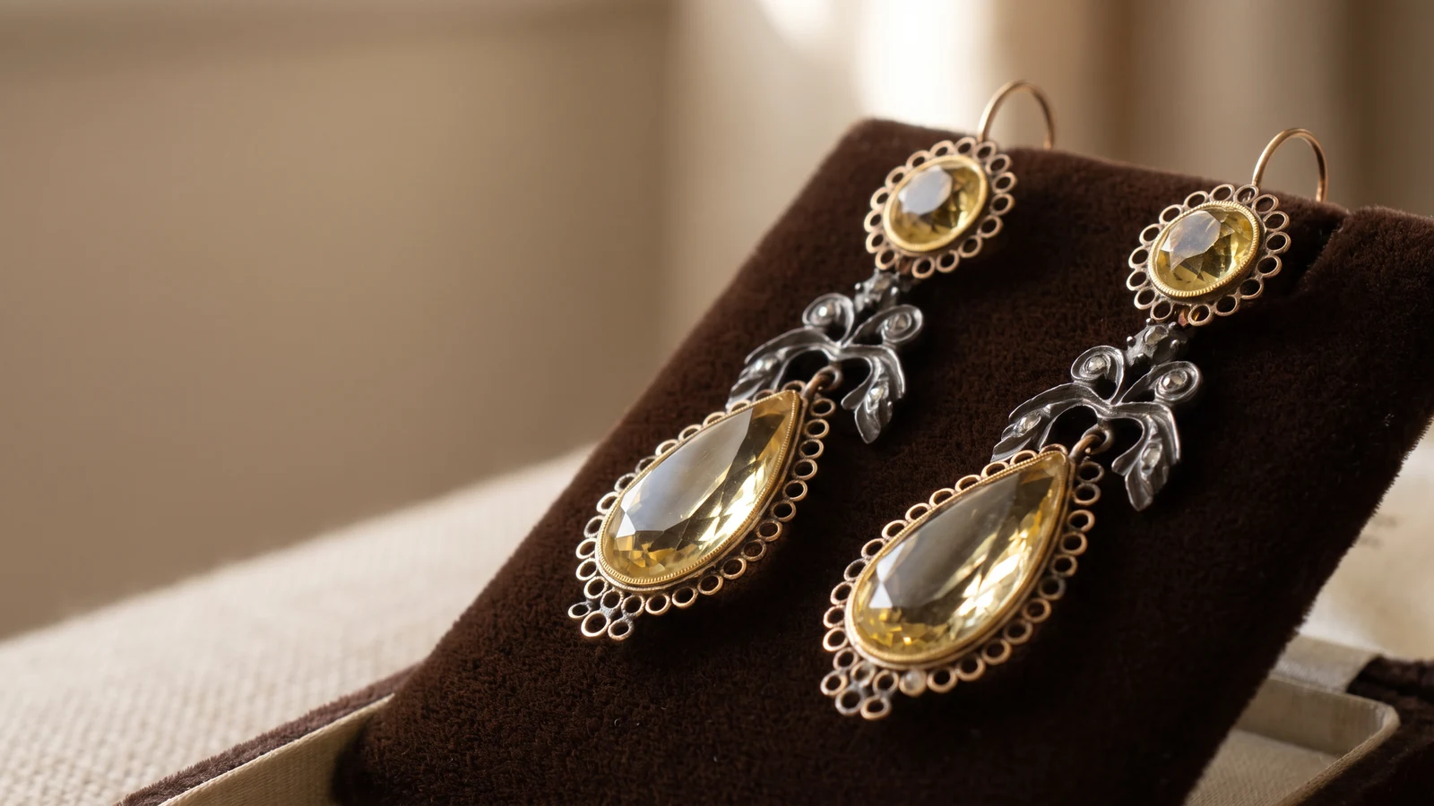 A pair of antique gold drop earrings on a dark velvet pad