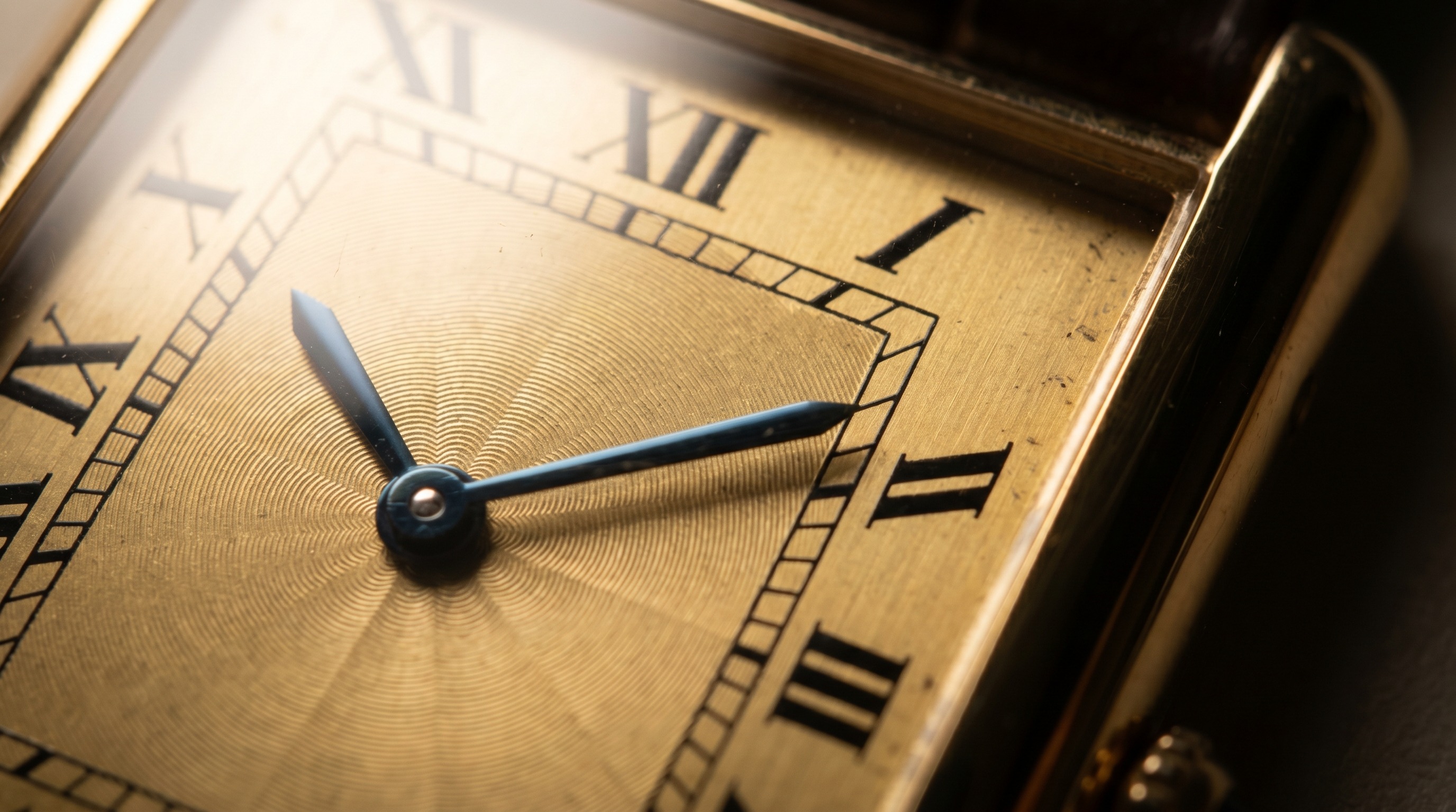 Macro of a rectangular gold Cartier Tank dial with Roman numerals, railway minute track and blued sword hands