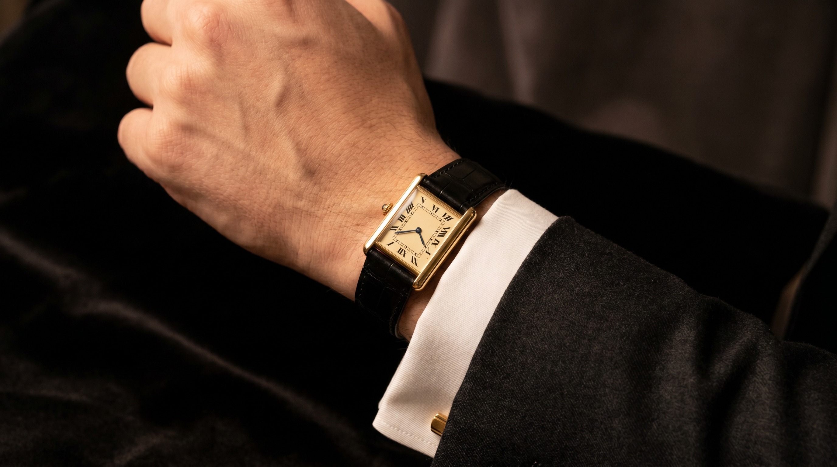 Slim gold Cartier Tank watch worn on the wrist with a white shirt cuff and dark suit