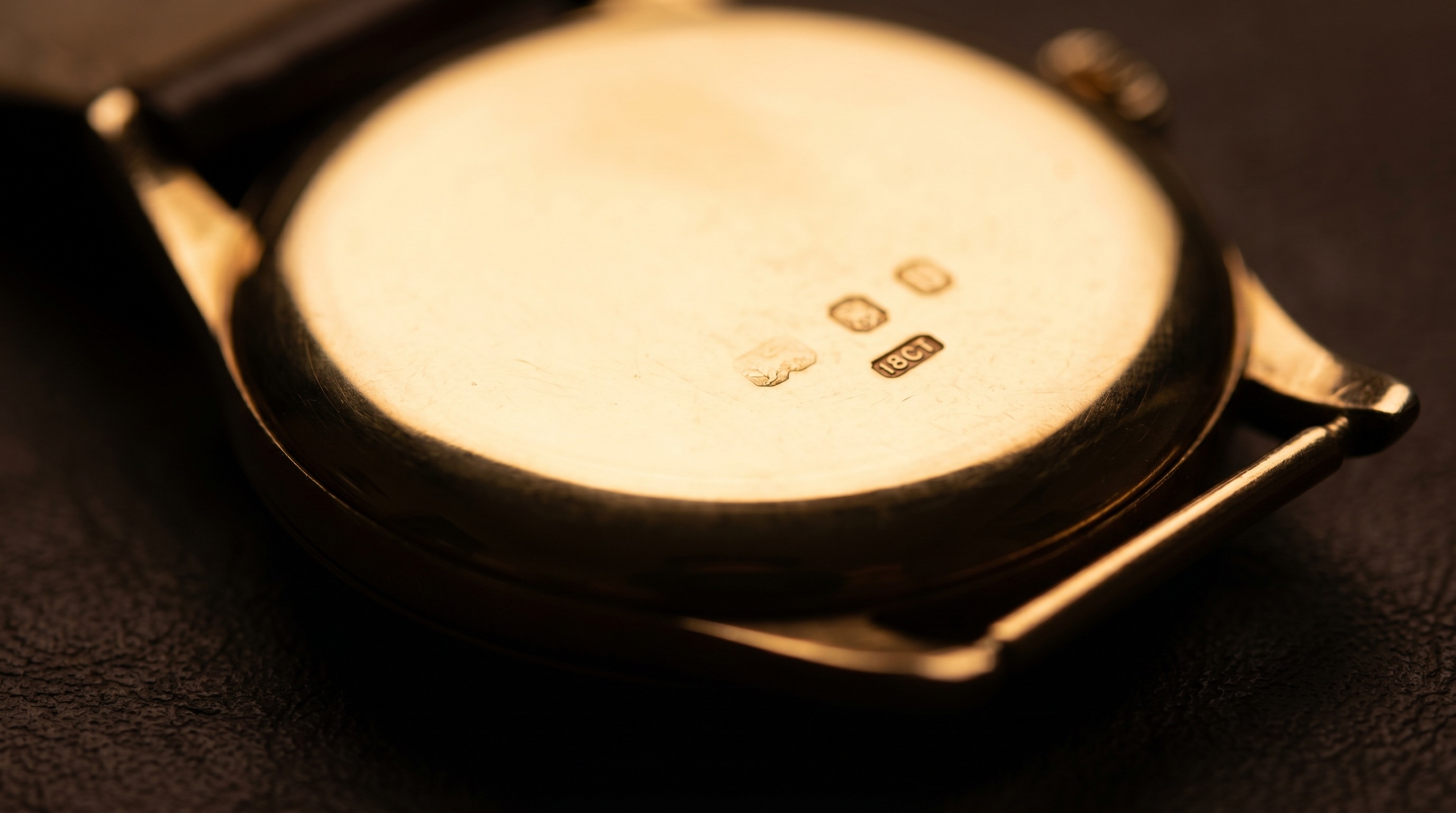 Polished gold watch case-back stamped with tiny 18ct hallmark punches